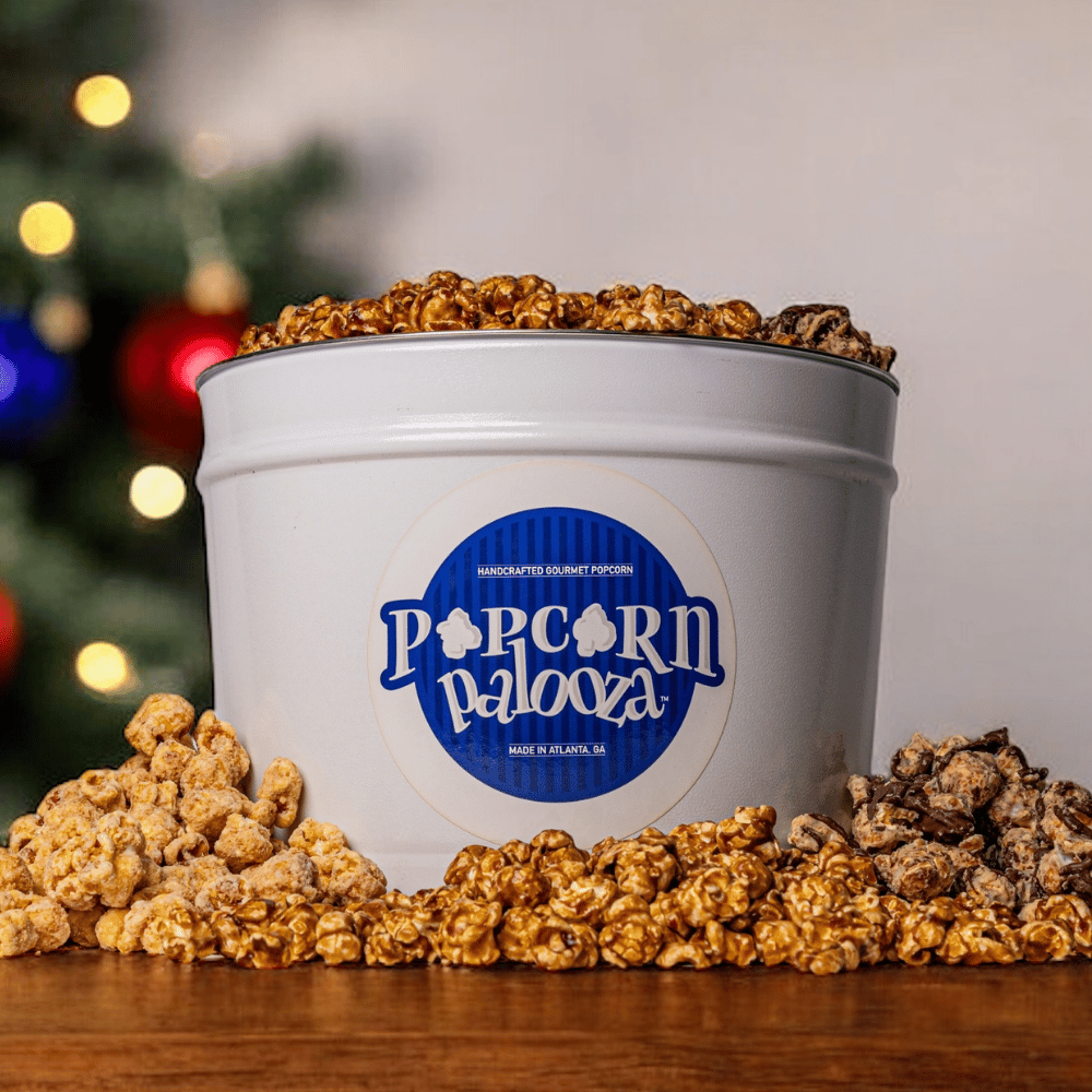 White bucket of popcorn with 'Popcorn Palooza' logo against a blurred Christmas tree background